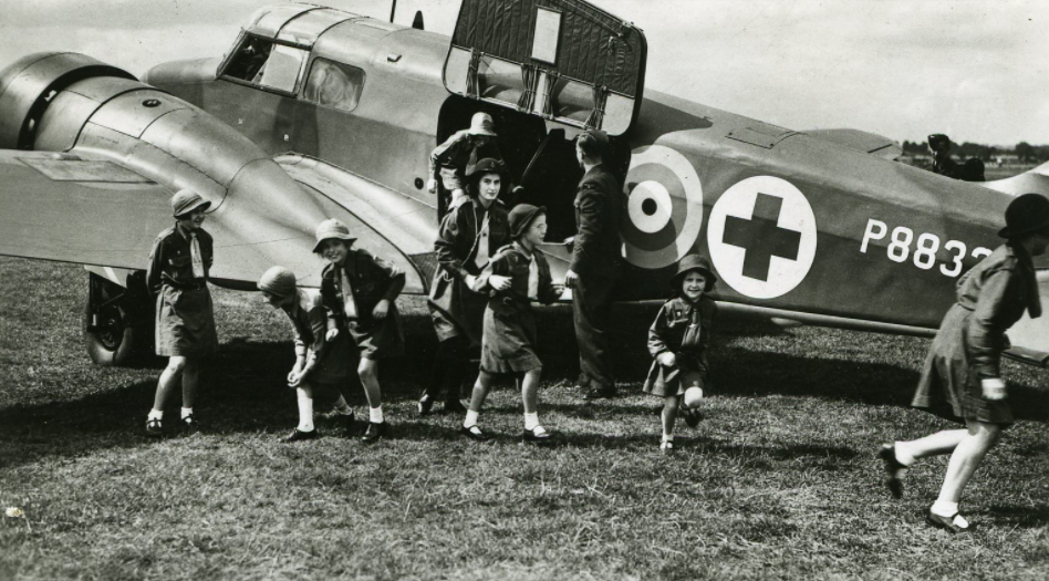 Black and white image of Girl Guides around a Spitfire.